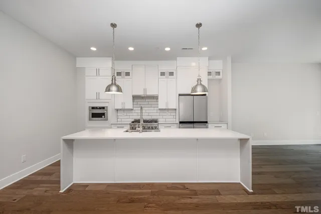 a large white kitchen with kitchen island a sink stainless steel appliances and white cabinets