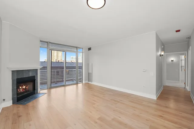 a view of an empty room with wooden floor fireplace and a window