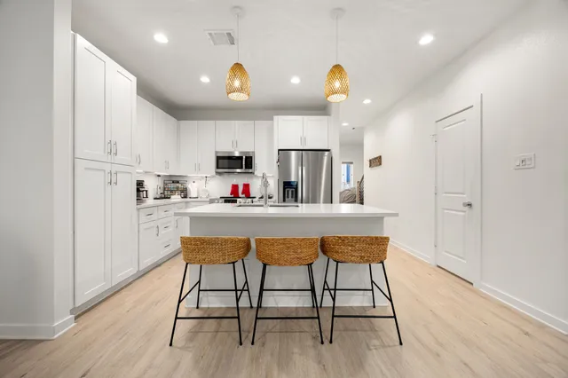 a kitchen with kitchen island stainless steel appliances a dining table chairs sink and cabinets
