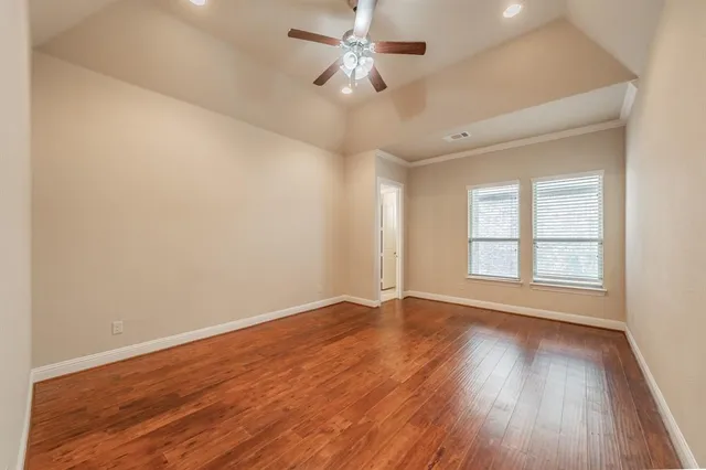 an empty room with wooden floor chandelier fan and windows