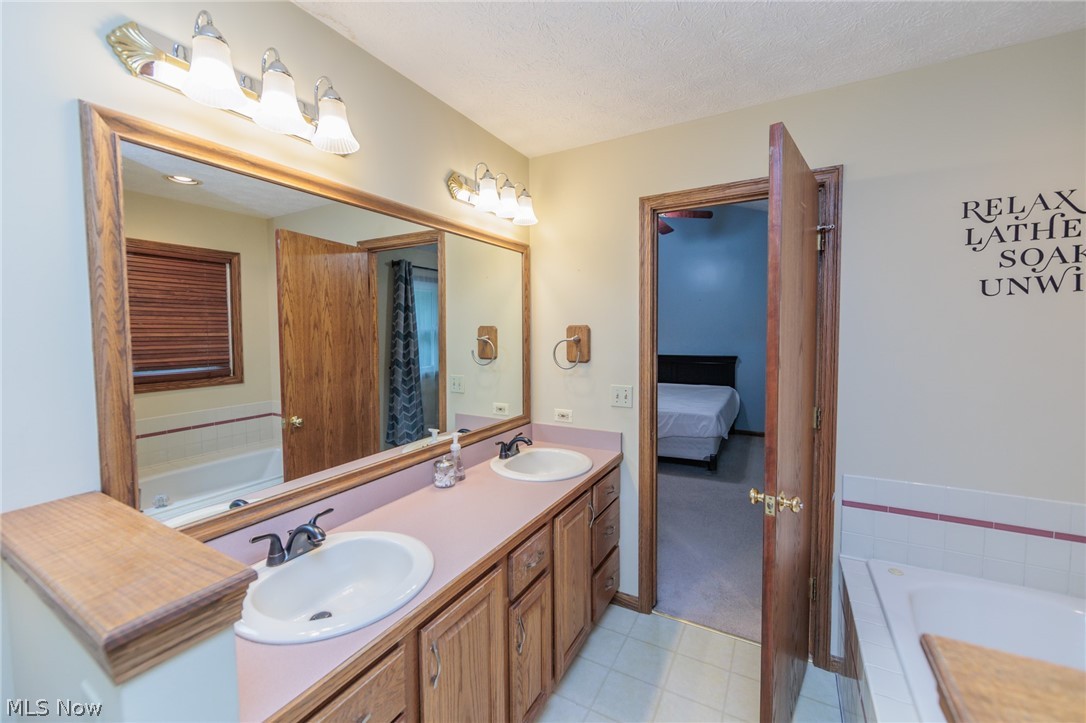 4123 Baird Road Stow, OH 44224 - Photo 23 of 47 Bathroom featuring a relaxing tiled tub, tile patterned flooring, dual vanity, and a textured ceiling