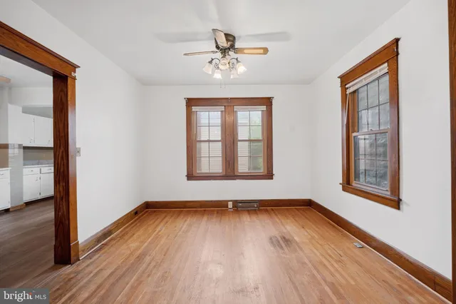 an empty room with wooden floor chandelier fan and windows
