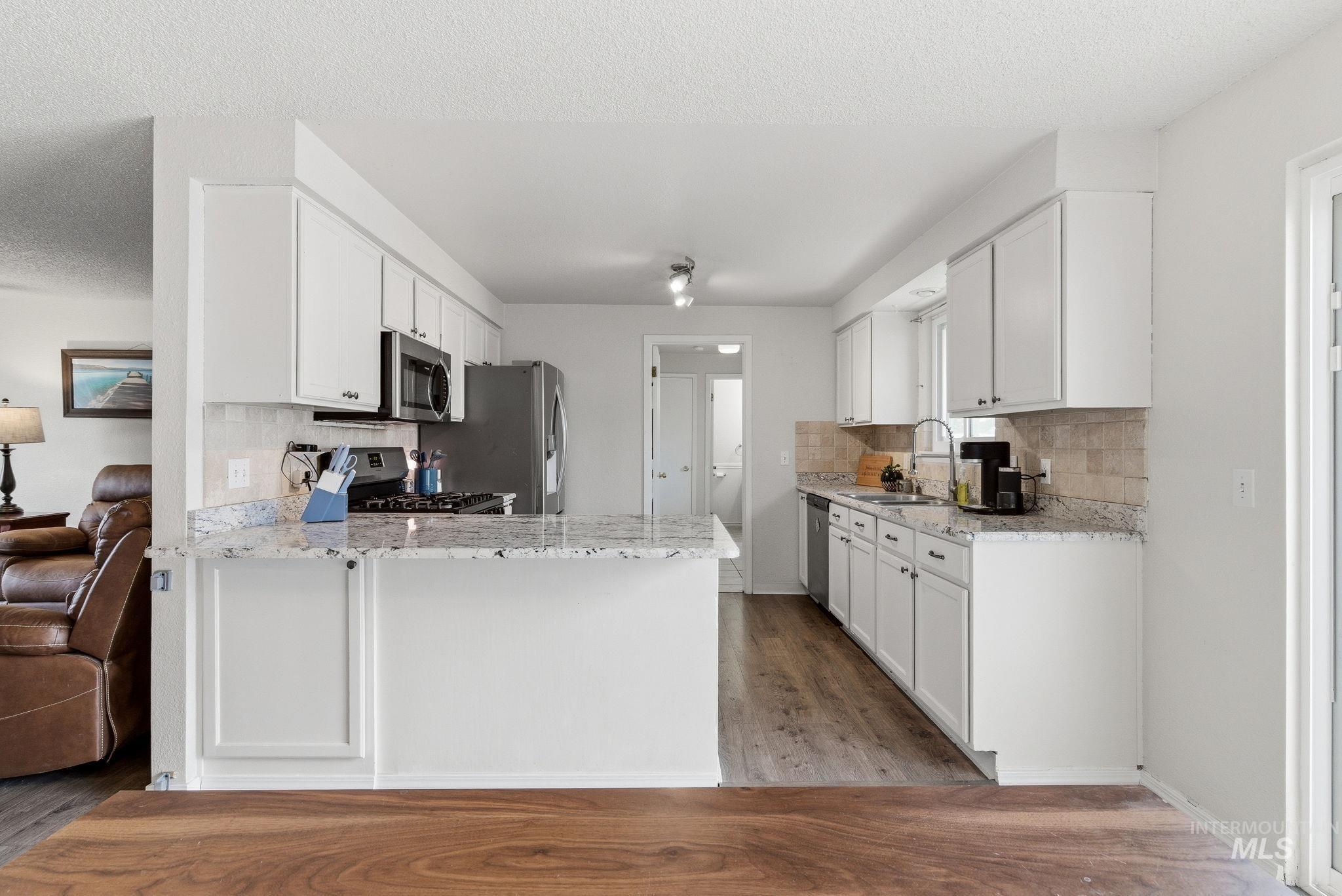 598 Easy Street Kuna, ID 83634 - Photo 12 of 50 Kitchen with backsplash, white cabinetry, light stone counters, a peninsula, and a textured ceiling
