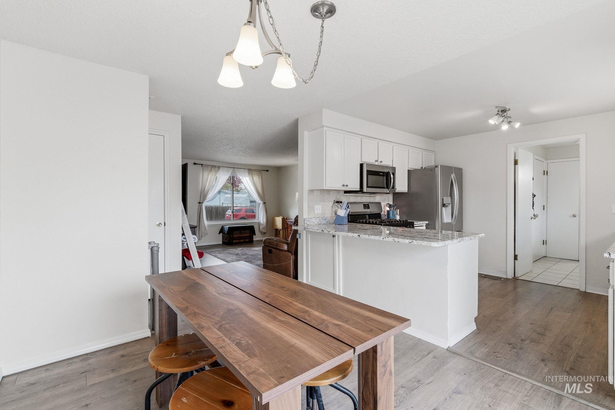 598 Easy Street Kuna, ID 83634 - Photo 13 of 50 Kitchen featuring white cabinets, light stone countertops, stainless steel appliances, light wood-type flooring, and suspended lighting