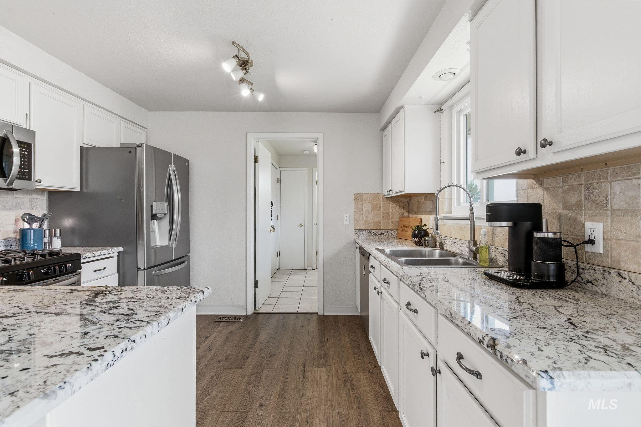 598 Easy Street Kuna, ID 83634 - Photo 14 of 50 Kitchen featuring backsplash, white cabinetry, light stone counters, stainless steel appliances, and dark wood-style flooring