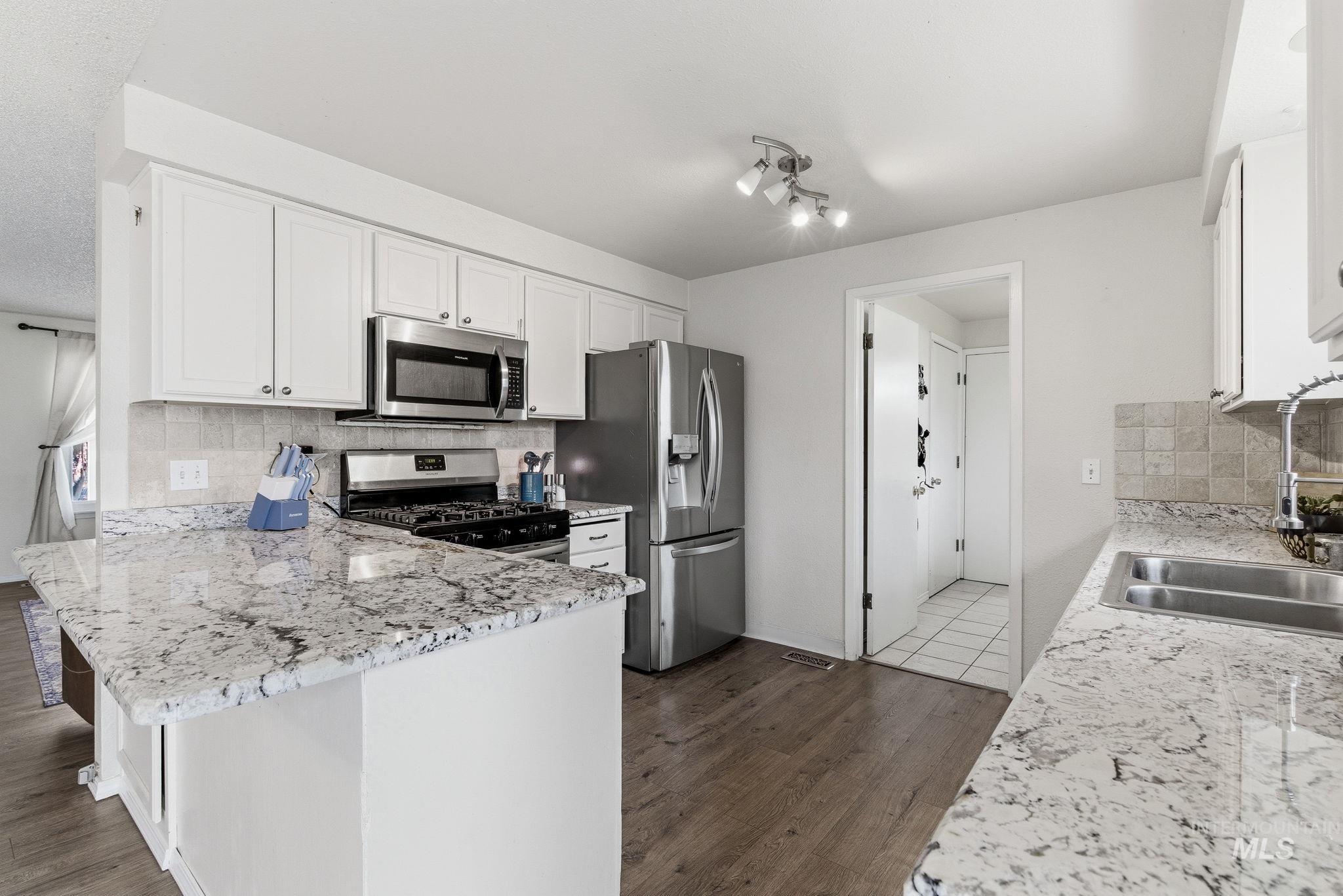 598 Easy Street Kuna, ID 83634 - Photo 16 of 50 Kitchen with decorative backsplash, white cabinetry, stainless steel appliances, a peninsula, and dark wood-type flooring