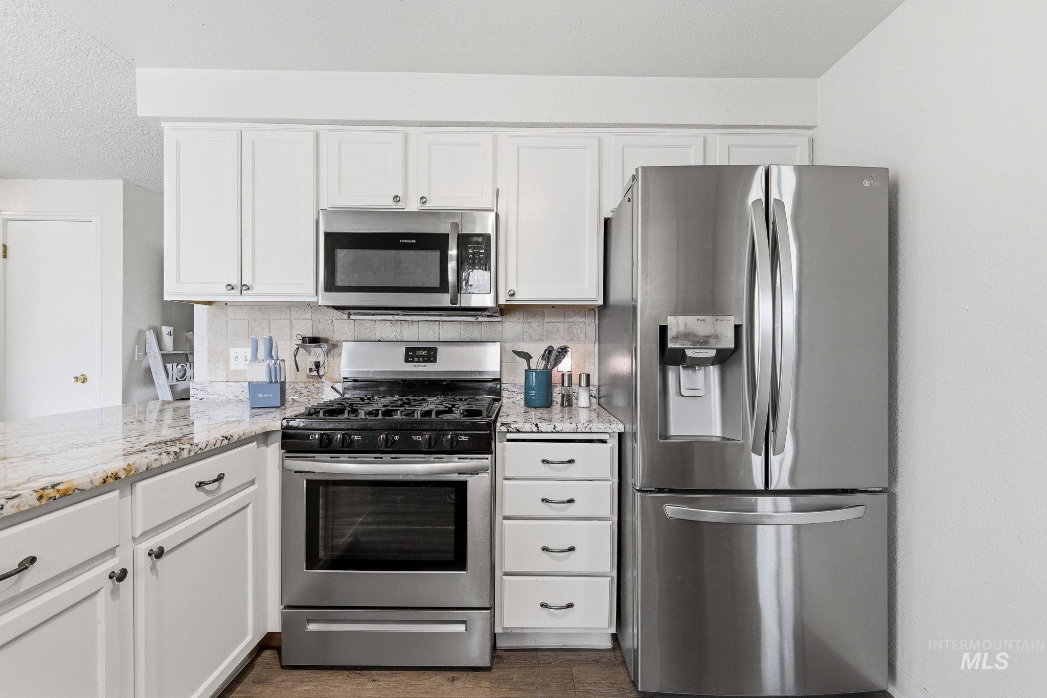 598 Easy Street Kuna, ID 83634 - Photo 18 of 50 Kitchen with stainless steel appliances, white cabinetry, light stone counters, and backsplash