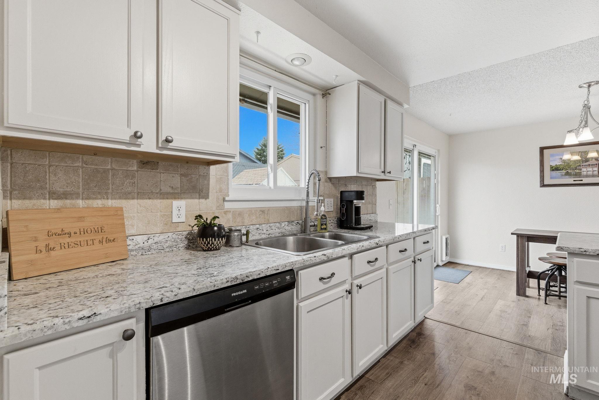 598 Easy Street Kuna, ID 83634 - Photo 22 of 50 Kitchen featuring backsplash, stainless steel dishwasher, white cabinetry, light wood-style floors, and suspended lighting