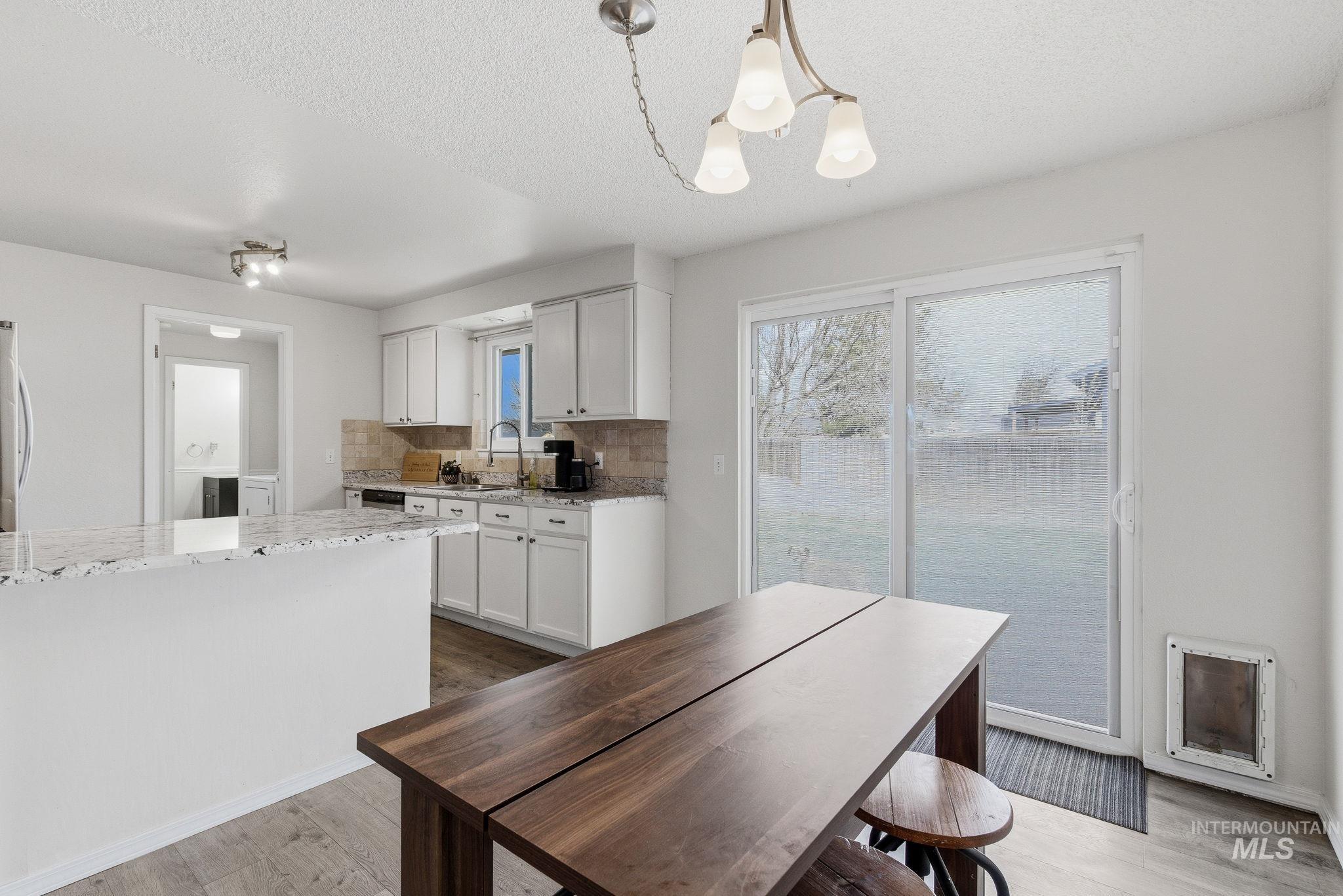 598 Easy Street Kuna, ID 83634 - Photo 25 of 50 Kitchen with light stone counters, tasteful backsplash, suspended lighting, light wood-type flooring, and white cabinetry