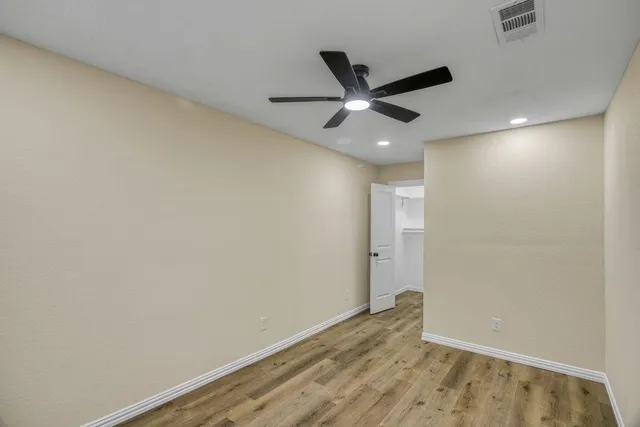 an empty room with wooden floor and a ceiling fan