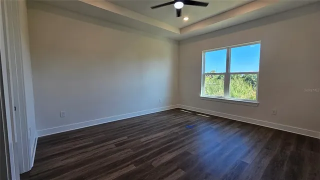 an empty room with wooden floor chandelier fan and windows