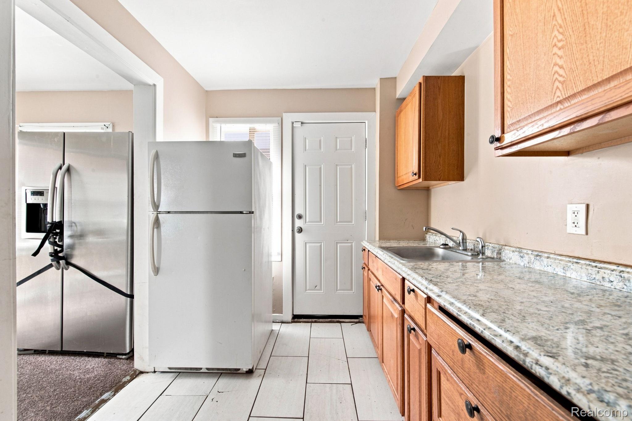 8882 Evergreen Road Detroit, MI 48228 - Photo 11 of 21 Kitchen featuring wood cabinetry, light-toned countertop, stainless steel sink, and white tile flooring