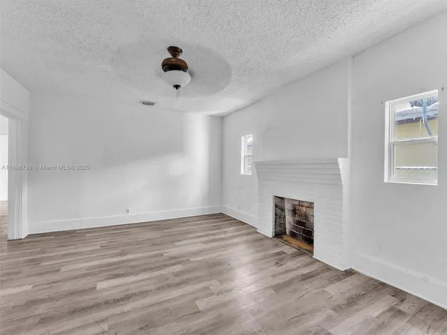 an empty room with wooden floor fireplace and windows