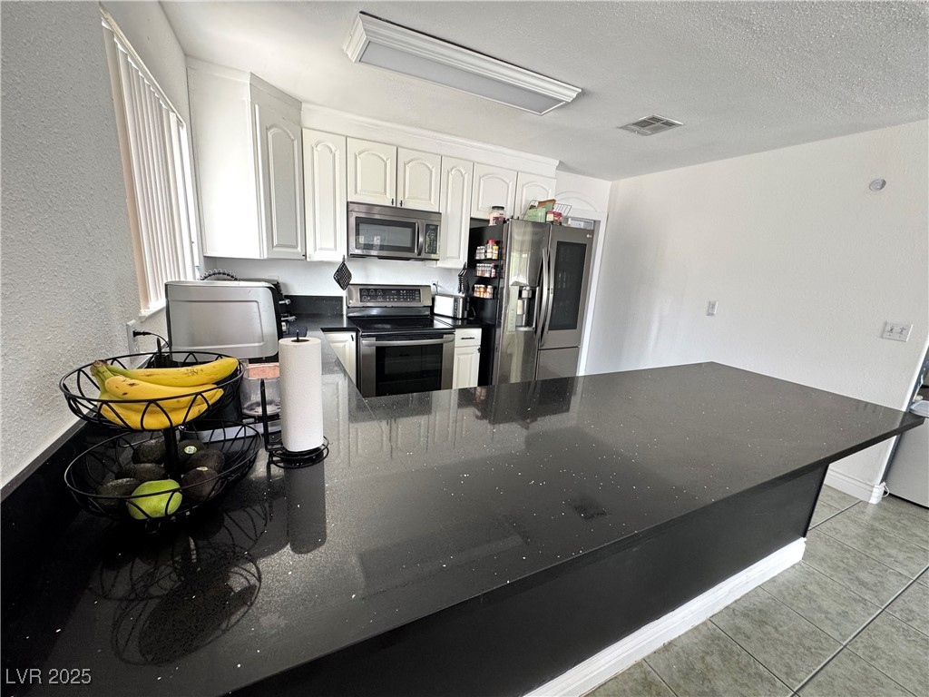 5248 Rambling Road Las Vegas, NV 89120 - Photo 4 of 33 Kitchen featuring a peninsula, appliances with stainless steel finishes, a textured wall, light tile patterned flooring, and white cabinetry
