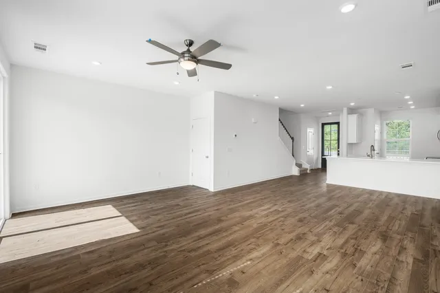 an empty room with wooden floor a ceiling fan and kitchen view