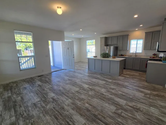a view of kitchen with kitchen island granite countertop wooden floor stainless steel appliances cabinets and living room