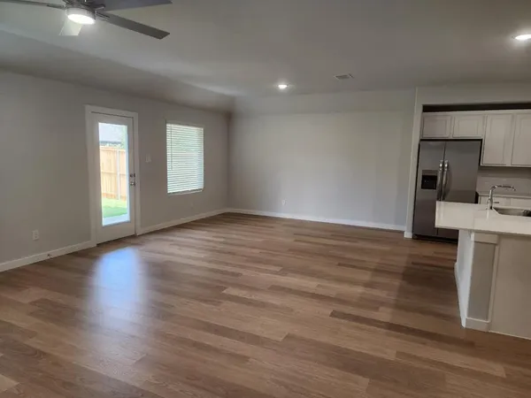 an empty room with wooden floor and a kitchen