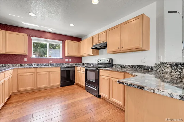 a kitchen with granite countertop a stove top oven a sink dishwasher and cabinets with wooden floor