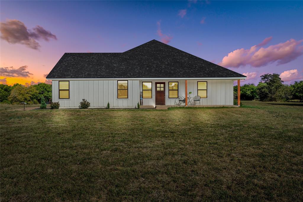 Modern farmhouse with a front yard, a porch, board and batten siding, and a shingled roof