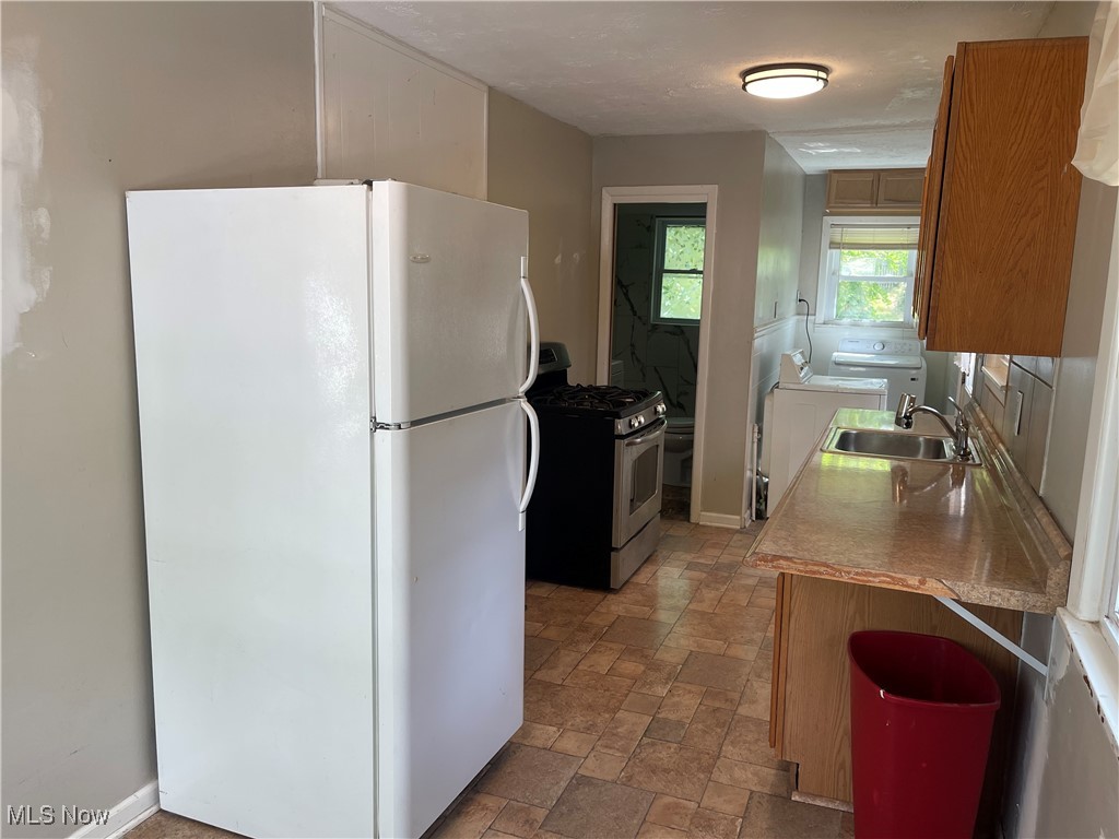 353 Gibbs Road Akron, OH 44312 - Photo 10 of 15 Kitchen with freestanding refrigerator, stainless steel gas stove, stone tile flooring, brown cabinets, and washing machine and dryer
