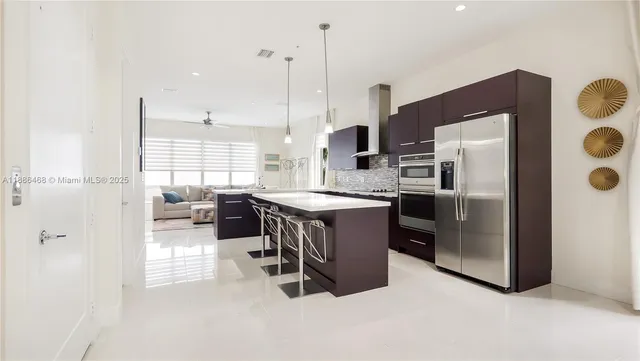 a kitchen with stainless steel appliances kitchen island granite countertop a refrigerator a stove a sink a dining table and chairs with wooden floor