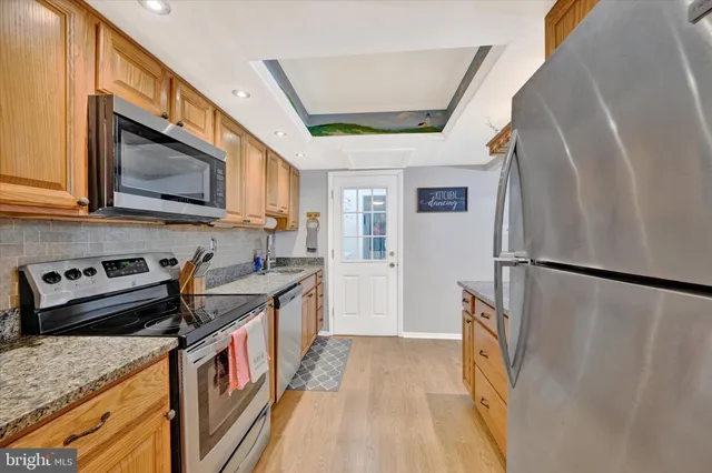 a kitchen with stainless steel appliances granite countertop a refrigerator a stove and a sink with wooden floor