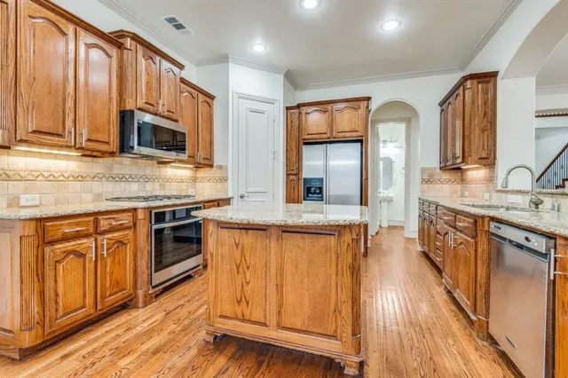 a kitchen with stainless steel appliances granite countertop wooden cabinets a sink and dishwasher a refrigerator with wooden floor