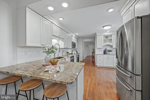 a kitchen with stainless steel appliances granite countertop a refrigerator a microwave oven a dining table and chairs with wooden floor