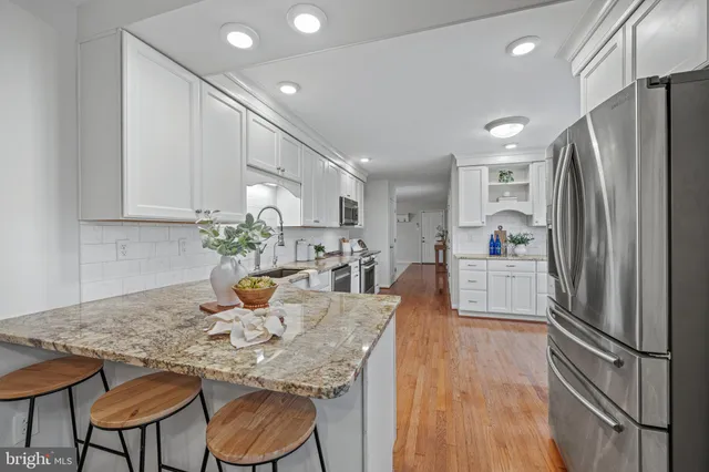 a kitchen with stainless steel appliances granite countertop a refrigerator a microwave oven a dining table and chairs with wooden floor