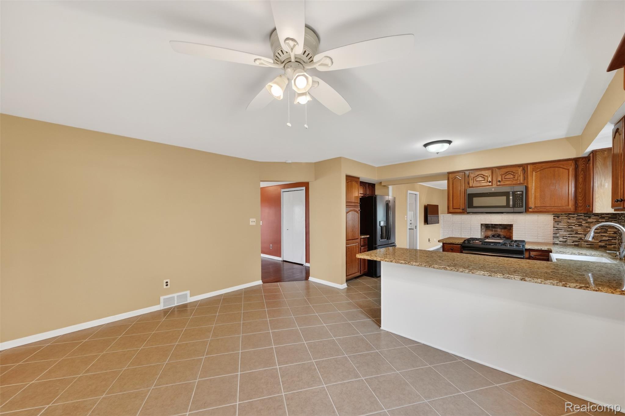 12014 Common Road Warren, MI 48093 - Photo 9 of 30 Kitchen with wood finish cabinetry, black stainless appliances, light stone countertops, a ceiling fan, and tasteful backsplash.
