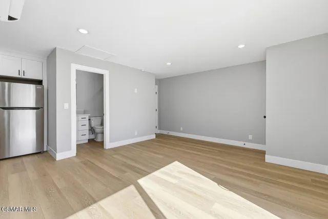 a view of empty room with wooden floor and kitchen