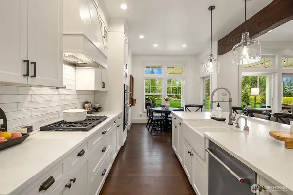 a large kitchen with stainless steel appliances a stove a sink a oven a dining table and chairs with wooden floor