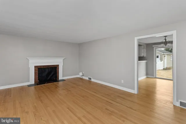 a view of an empty room with wooden floor fireplace and a window
