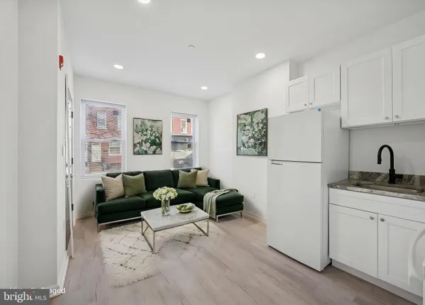 a living room with furniture a refrigerator a sink a window and white cabinets