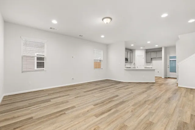 a view of an empty room with wooden floor and kitchen view