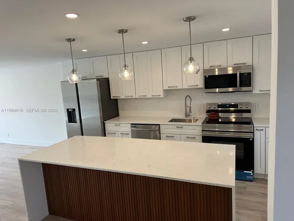 a kitchen with stainless steel appliances a stove a sink a microwave a refrigerator and white cabinets