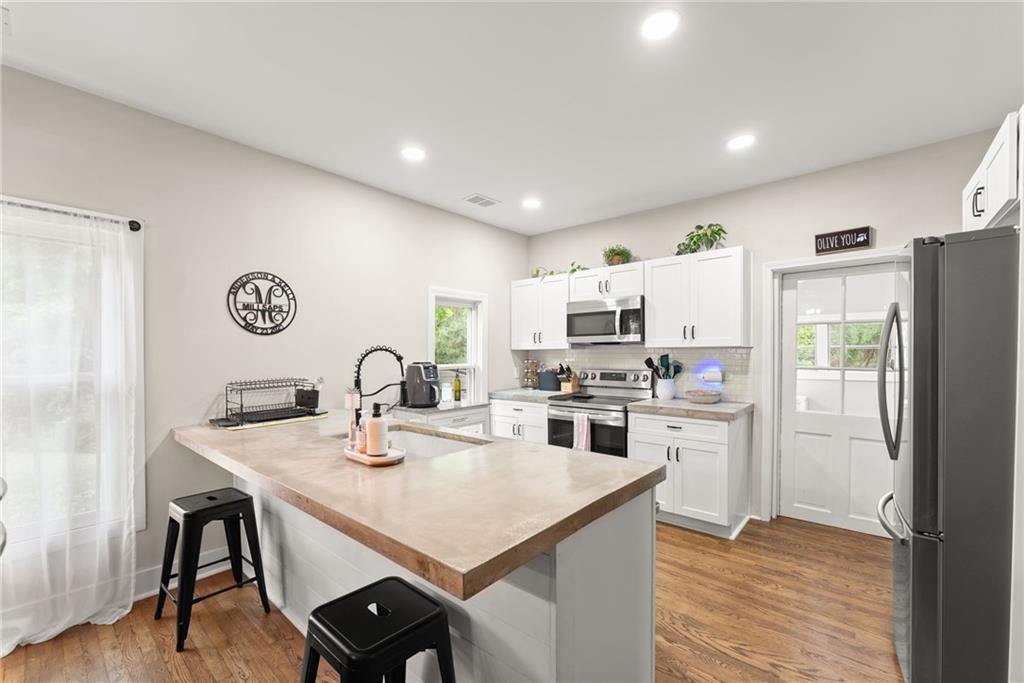 1519 New Hope Church Road Loganville, GA 30052 - Photo 11 of 48 a kitchen with stainless steel appliances granite countertop a stove a refrigerator a kitchen island a dining table and chairs with wooden floor