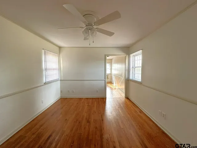 an empty room with wooden floor fan and windows
