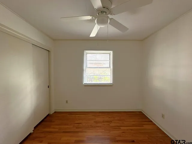 an empty room with wooden floor fan and windows