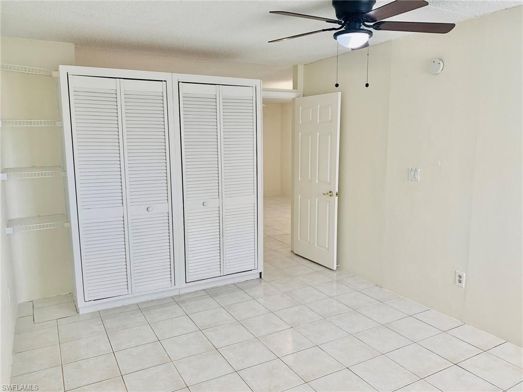 826 Wiggins Pass Road, Unit 214 Naples, FL 34110 - Photo 13 of 21 Unfurnished bedroom featuring a ceiling fan, a textured ceiling, light tile patterned floors, and two closets