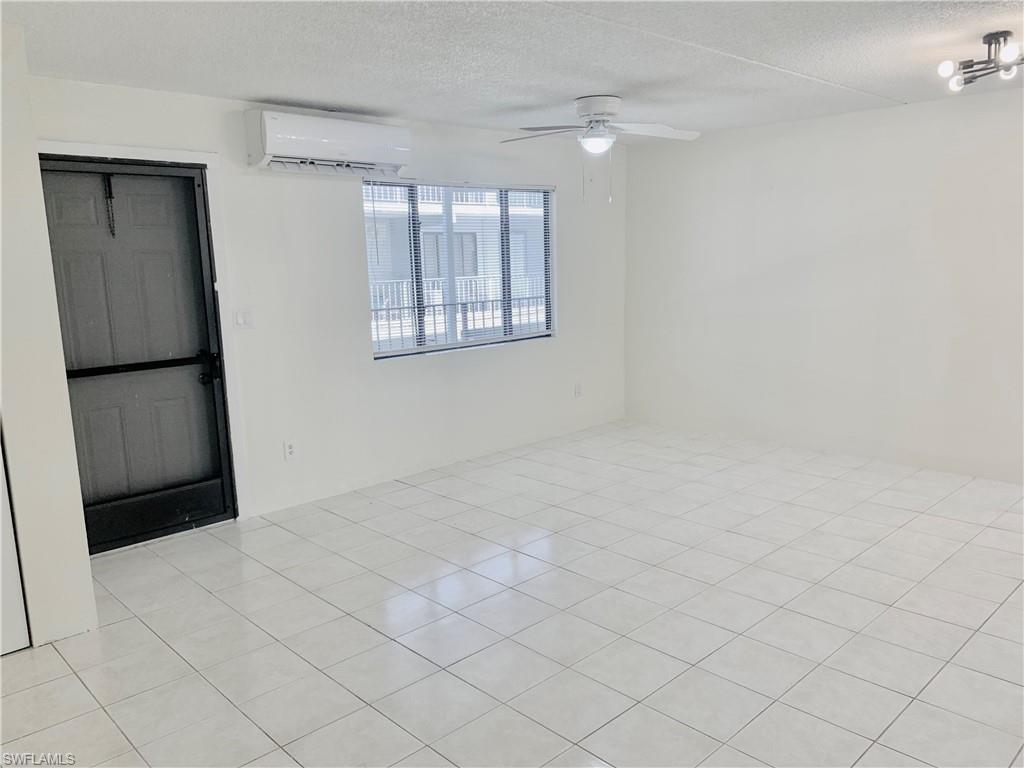 826 Wiggins Pass Road, Unit 214 Naples, FL 34110 - Photo 3 of 21 Spare room with a textured ceiling, a wall mounted air conditioner, light tile patterned flooring, and ceiling fan
