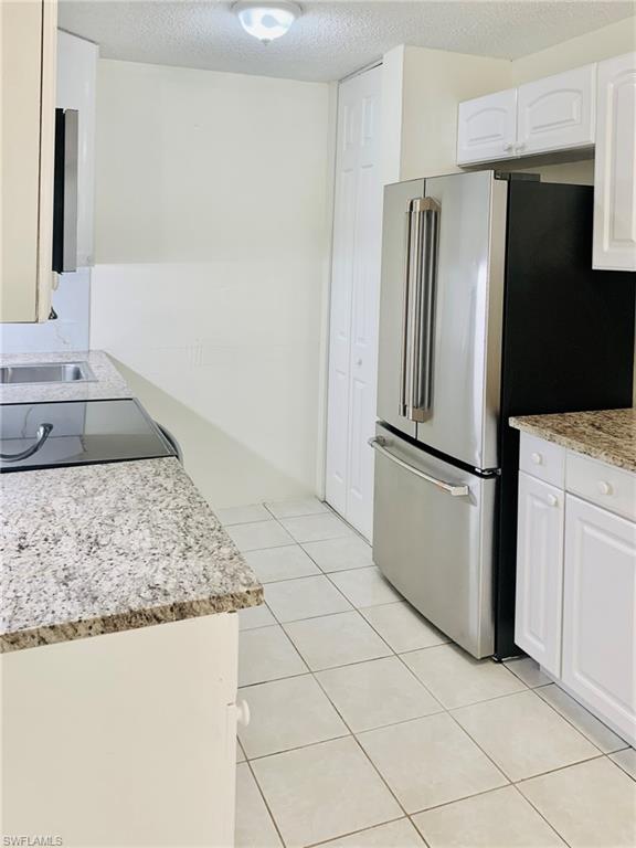 826 Wiggins Pass Road, Unit 214 Naples, FL 34110 - Photo 7 of 21 Kitchen featuring freestanding refrigerator, a textured ceiling, light stone counters, white cabinets, and black range with electric stovetop