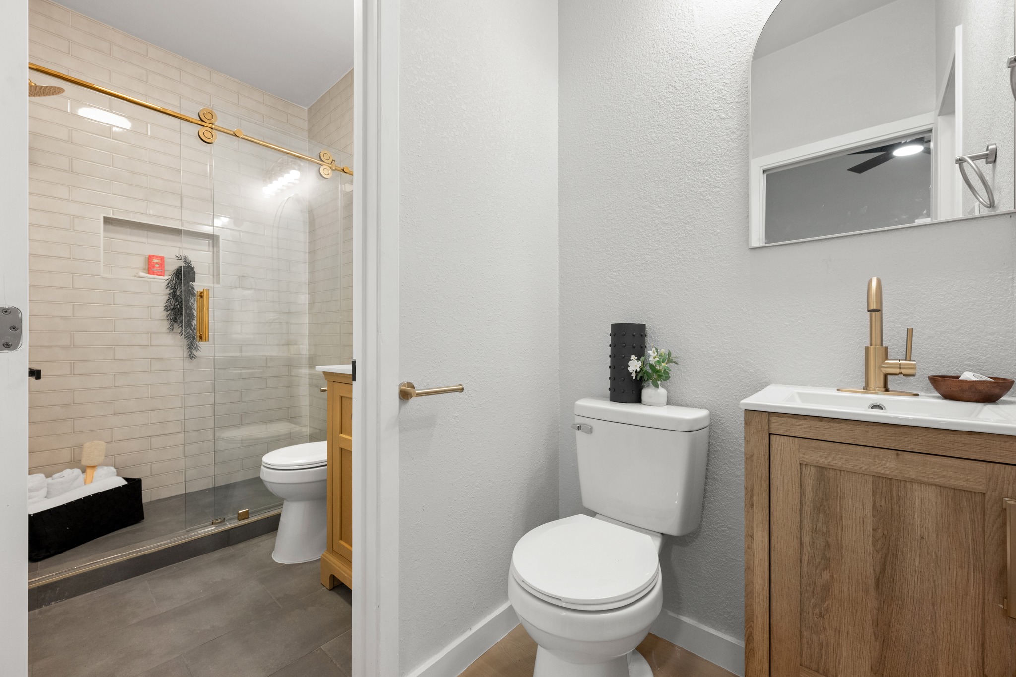 6501 Brush Country Road, Unit 120 Austin, TX 78749 - Photo 15 of 26 Modern half bathroom featuring a wood-finish vanity with an integrated sink, a gold-tone faucet, and an arched mirror as well as direct access to the full bathroom
