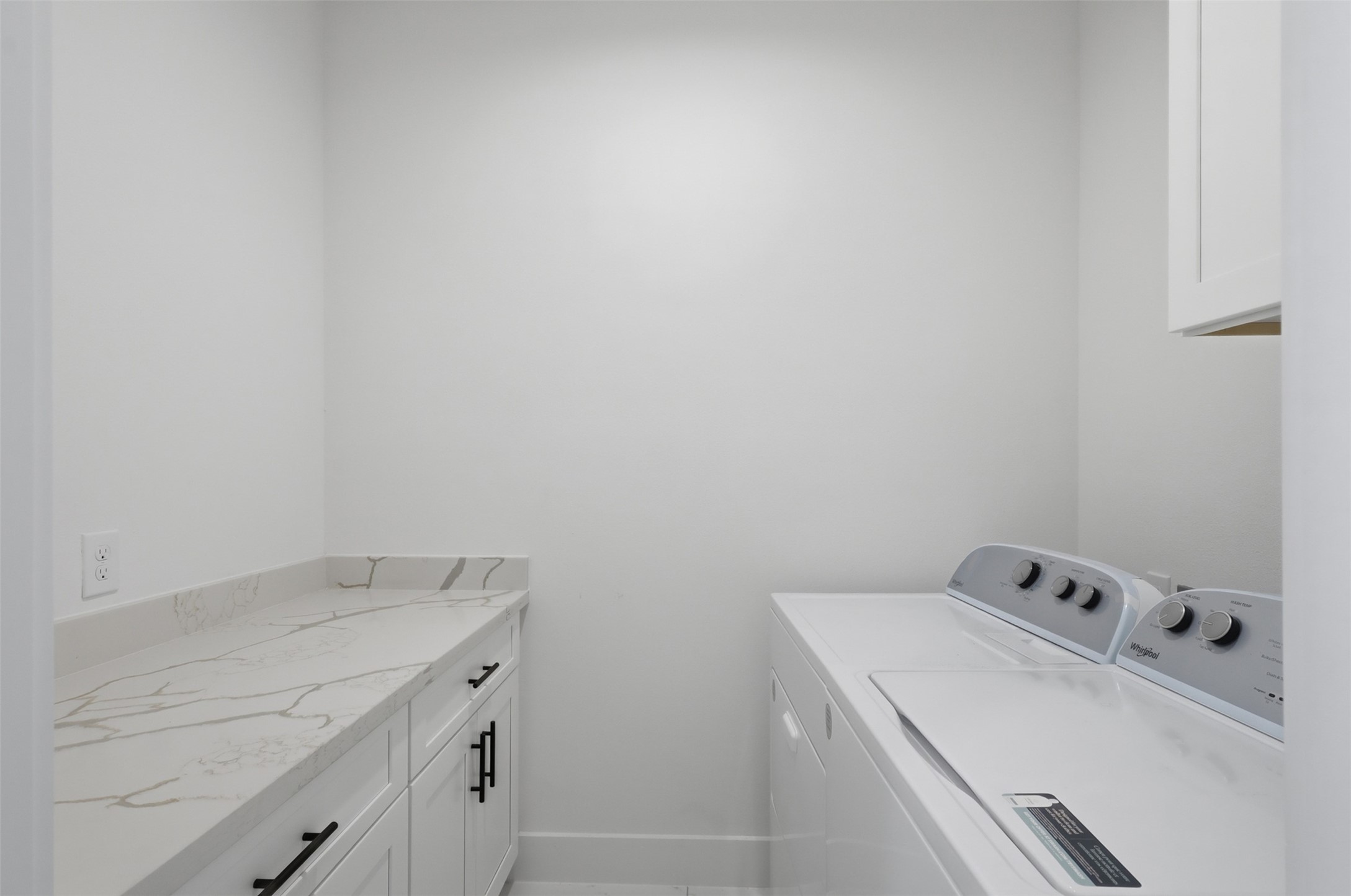 6833 Paris Street Houston, TX 77021 - Photo 11 of 23 This is a clean, modern laundry room featuring a washer and dryer, with white cabinetry and a marble-patterned countertop, providing ample workspace and storage.