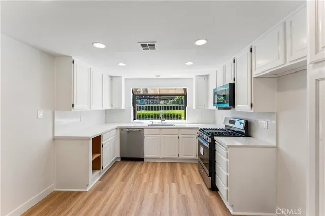 a kitchen with granite countertop a sink stove refrigerator and white cabinets with wooden floor