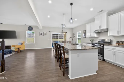 a kitchen with stainless steel appliances granite countertop a stove top oven a sink a dining table and chairs with wooden floor
