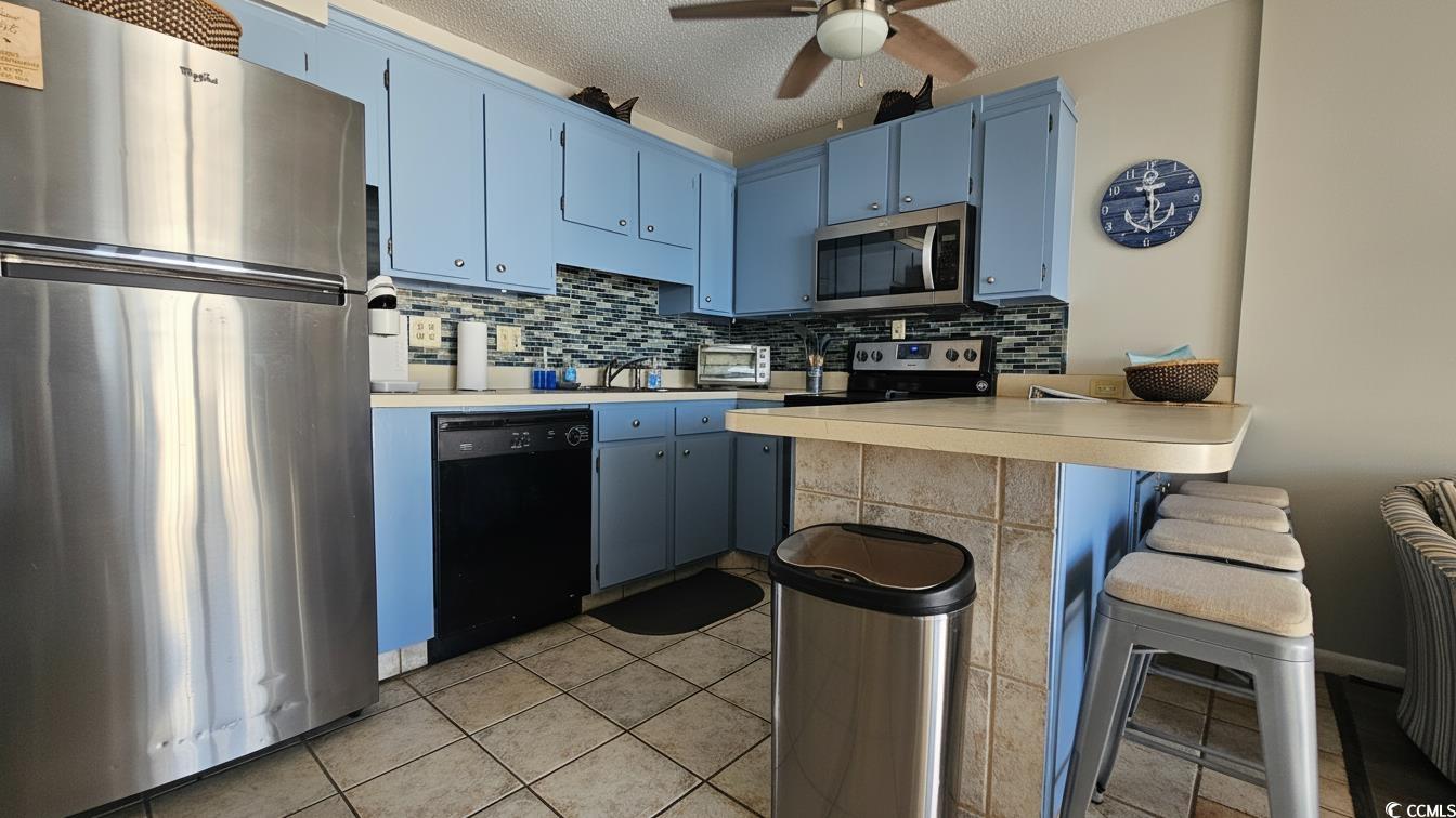 1210 North Waccamaw Drive, Unit 512 Murrells Inlet, SC 29576 - Photo 10 of 20 Kitchen featuring appliances with stainless steel finishes, a kitchen breakfast bar, blue cabinets, light countertops, and a peninsula