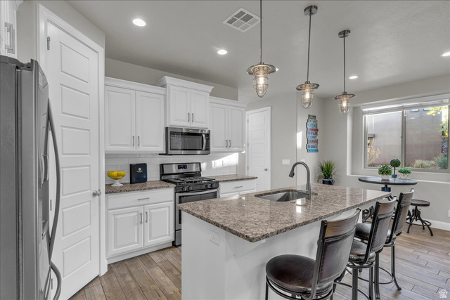 4796 Winged Foot Drive St. George, UT 84770 - Photo 21 of 33 Kitchen with stainless steel appliances, a kitchen island with sink, white cabinets, and light wood finished floors