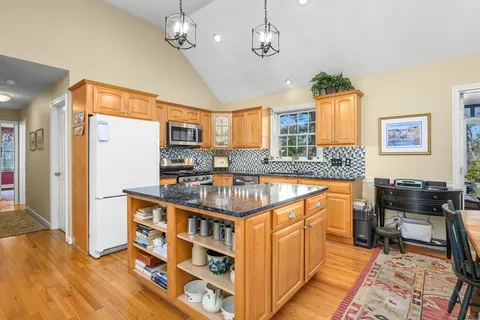 a very nice looking kitchen with granite countertop a stove refrigerator and a dining table with wooden floor