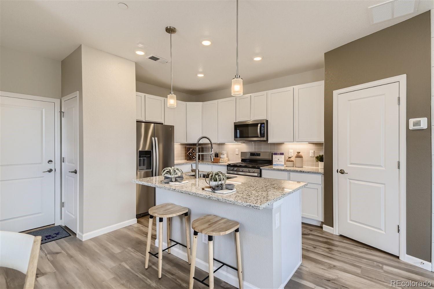 450 Millwall Circle Castle Pines, CO 80108 - Photo 7 of 23 a kitchen with kitchen island a refrigerator stove and white cabinets with wooden floor
